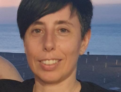 Persona sorridente con capelli corti, sfondo di spiaggia al tramonto.