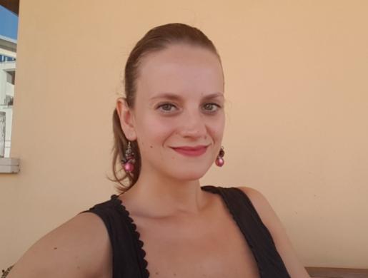 Donna sorridente con orecchini rosa, indossa un top nero, sfondo beige.