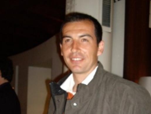 Uomo sorridente con giacca scura in un ambiente interno.