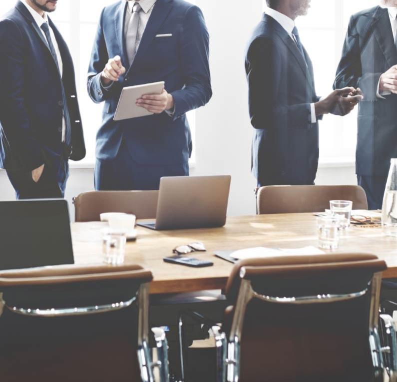 Uomini in abiti formali discutono attorno a un tavolo da riunione.